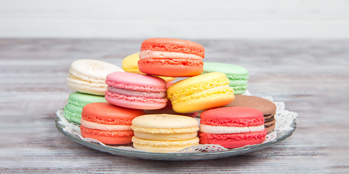Colored macaroons pastel colors with different flavors on glass plate with paper towel. Bright and delicious dessert/ Wooden background