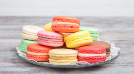 Colored macaroons pastel colors with different flavors on glass plate with paper towel. Bright and delicious dessert/ Wooden background