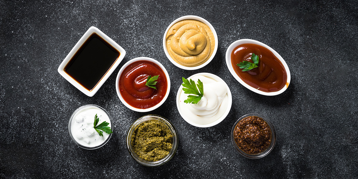 Set of sauces - ketchup, mayonnaise, mustard soy sauce, bbq sauce, pesto, mustard grains and pomegranate sauce on dark stone table. Top view.