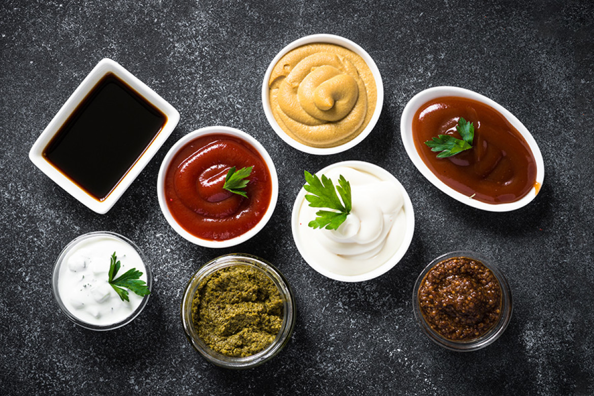 Set of sauces - ketchup, mayonnaise, mustard soy sauce, bbq sauce, pesto, mustard grains and pomegranate sauce on dark stone table. Top view.