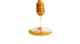 Honey dripping from a wooden honey dipper isolated on white background